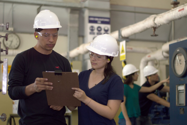 Two engineers are discussing about a industrial project at a site, engineering equipment can be seen around.