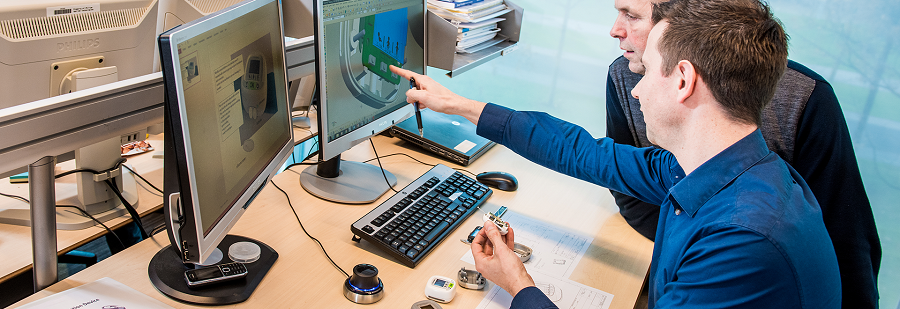 Two persons sitting on their respective chairs and pointing to a computer which shows a picture of a product design.